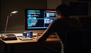 Back view of a programmer sitting and writing code in a dark room